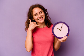 Young caucasian woman holding a clock isolated on yellow background showing a mobile phone call gesture with fingers.