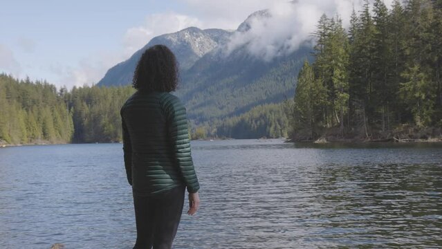 Adventurous Caucasian Woman on the rocks by the water in Canadian Nature Landscape. Buntzen Lake, Anmore, Vancouver, BC, Canada. Adventure Travel Concept