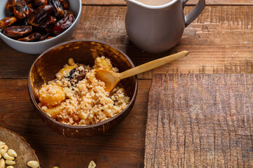 A plate of couscous with saffron and nuts on a wooden table next to dates and a jug of fruit broth.
