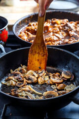 Fried champignon mushrooms with onions in a frying pan with a wooden spatula stirs a female hand.
