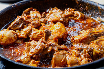 Fried chicken in spices and sauce is hot in a frying pan.