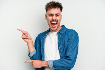 Young caucasian man isolated on white background pointing with forefingers to a copy space,...