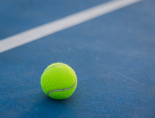 Close up of yellow tennis ball on a blue hard court.