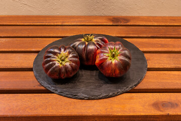 Plate with three tomatoes of the blue variety, ripe and ready to eat on a wooden table