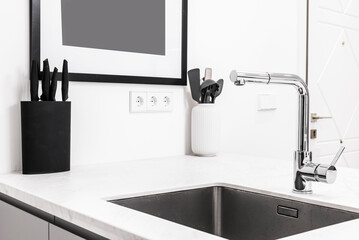 Corner of a kitchen with a white marble countertop, a built-in stainless steel sink and a knife rack with black handles