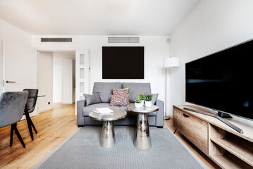 Living room and dining room with gray sofa, large tv on wooden sideboard, silver side coffee tables and wooden floors