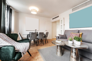 Living room and dining room with gray sofa, large TV on wooden sideboard, silver coffee tables, artificial plants, glass dining table and hardwood floors
