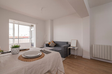Living room and dining room with gray sofa, table with beige linen tablecloth and light wood flooring