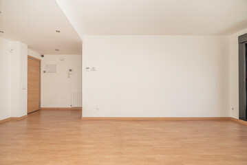 Fototapeta na wymiar Empty living room of an apartment with wooden floors, white aluminum radiators, freshly painted walls in plain white color and access door in beech wood color