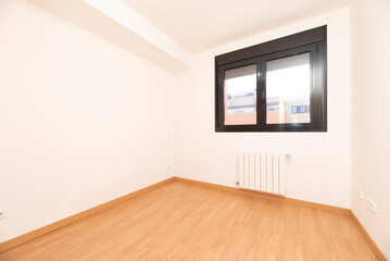 Unfurnished bedroom with beech-colored parquet floors, matching skirting boards, dark brown aluminum window and white aluminum radiator below