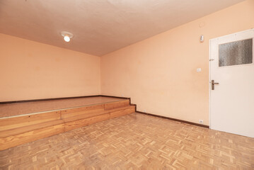 Empty room with white wooden door and glass skylight, peach painted walls, raised floor and oak...