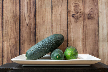 White porcelain tray with unpeeled green salad cucumbers on a wooden background
