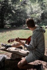 Unrecognizable young man playing guitar sitting in the nature surrounded by trees
