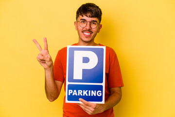 Young hispanic man holding parking placard isolated on yellow background showing number two with fingers.