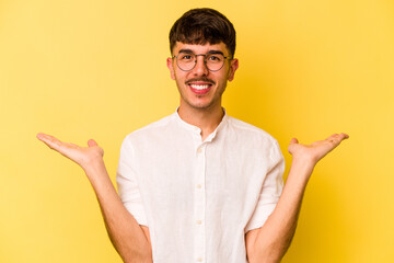 Young caucasian man isolated on yellow background makes scale with arms, feels happy and confident.