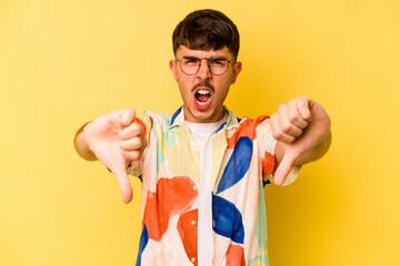 Young caucasian man isolated on yellow background showing thumb down and expressing dislike.
