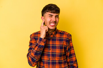 Obraz premium Young caucasian man isolated on yellow background covering ears with fingers, stressed and desperate by a loudly ambient.