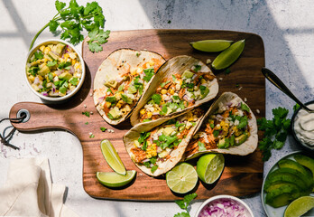 Overhead of soft tacos with chicken, corn, avocado and lime.