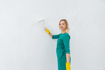 A young girl is engaged in repairs and paints a white wall with a roller in a new apartment. Renovation of the interior and a new apartment. Housewarming and a desirable mortgage.