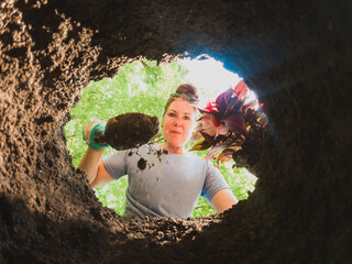 Woman planting a flower shot from inside the soil lined hole.