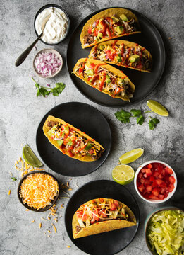 Hard shell tacos on plates with beef, lettuce, tomatoes, cheese.