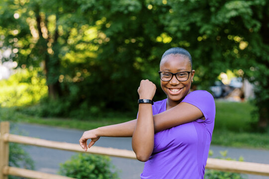 smiling teenage girl with glasses stretching shoulders outside