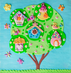 Clay handmade childish  illustration tree with birdhouses with birds, chips, nestlings singing songs spring time. Butterflies, free nature on a blue sky and green grass.