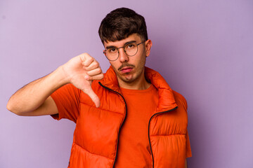 Young caucasian man isolated on purple background showing a dislike gesture, thumbs down....