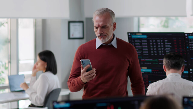 Mature entrepreneur look at cellphone screen feeling stressed standing in modern office