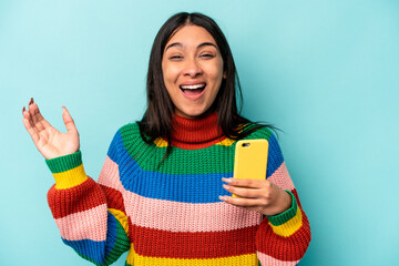 Young caucasian woman holding mobile phone isolated on blue background receiving a pleasant...