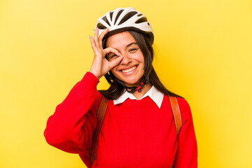 Young student hispanic woman wearing a bike helmet isolated on yellow background excited keeping ok gesture on eye.