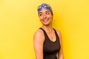 Young swimmer hispanic woman isolated on yellow background looks aside smiling, cheerful and pleasant.