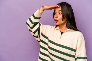 Young hispanic woman isolated on purple background looking far away keeping hand on forehead.