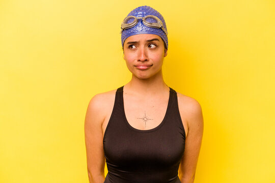 Young swimmer hispanic woman isolated on yellow background confused, feels doubtful and unsure.