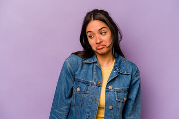 Fototapeta premium Young hispanic woman isolated on purple background shrugs shoulders and open eyes confused.