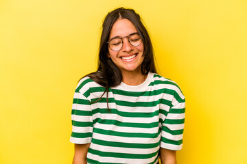 Young hispanic woman isolated on yellow background laughs and closes eyes, feels relaxed and happy.