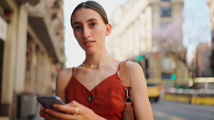 Сlose-up smiling young woman stands and looks at a map on a mobile phone. Girl stands on the street of the downtown scrolls the map on the smartphone.