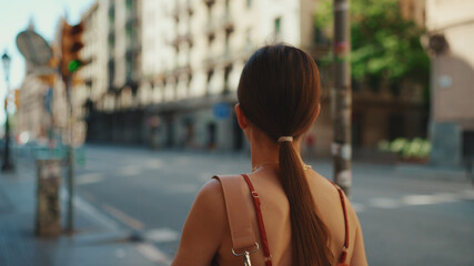 Beautiful young woman is walking down the street and sightseeing. Girl goes along a narrow street in the downtown and looks around carefully