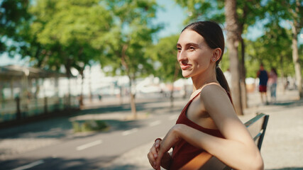 Fototapeta premium Pretty woman sitting on a park bench enjoying the good weather. Girl is resting on a park bench on urban background.