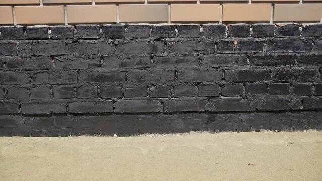 The bottom of the house, painted in a black house. Waterproofing the foundation of the house. Black bituminous mortar outside the house.
