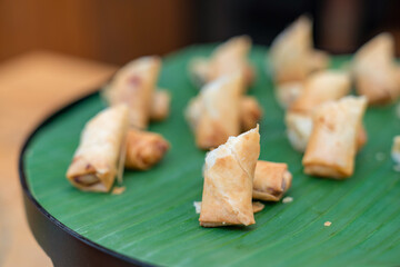 Deep fried spring roll vegetable and vermicelli on circle black plate with banana leaf at an outdoor wood table.