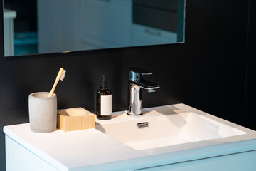 minimal toiletries such as toothbrush, serum bottle and wood storage on white sink and mirror on...