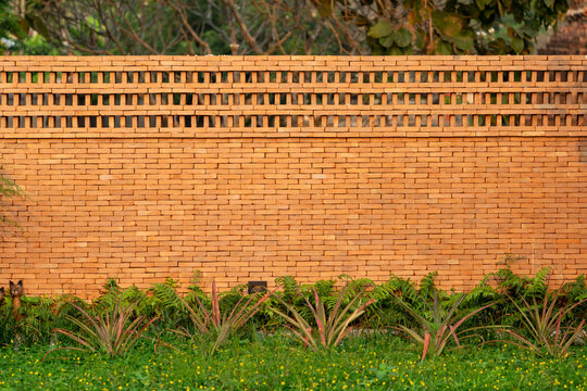 The brick wall, fence barrier is designed with a hole on top of wall in Asian style with garden grass field in the foreground