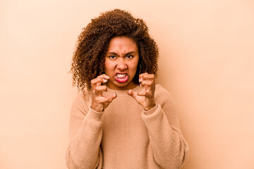 Young African American woman isolated on beige background upset screaming with tense hands.