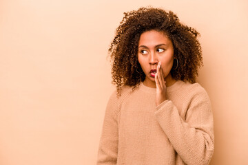 Young African American woman isolated on beige background is saying a secret hot braking news and looking aside