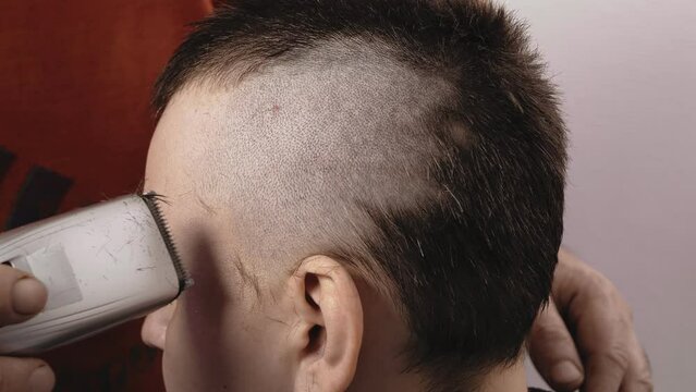 A man barber shaves a woman with a machine leaving a mohawk. Close-up