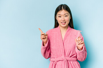 Young asian woman holding razor blade isolated on blue background smiling and pointing aside, showing something at blank space.