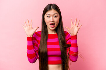 Young Chinese woman isolated on pink background receiving a pleasant surprise, excited and raising hands.