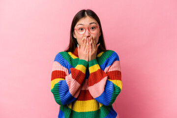 Young Chinese woman isolated on pink background shocked covering mouth with hands.