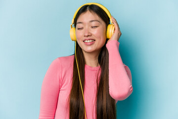 Young asian woman listening to music isolated on blue background